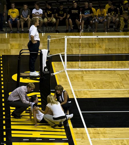 Volleyball officials:First referee waits while an injured players gets attended to.
