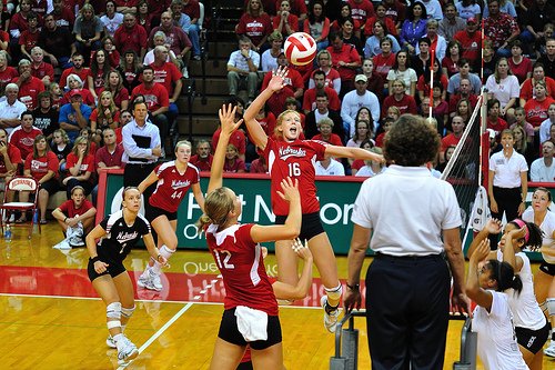 (John Carrel) Front row Nebraska setter runs a quick attack to her middle blocker while opposing team blockers wait and watch.